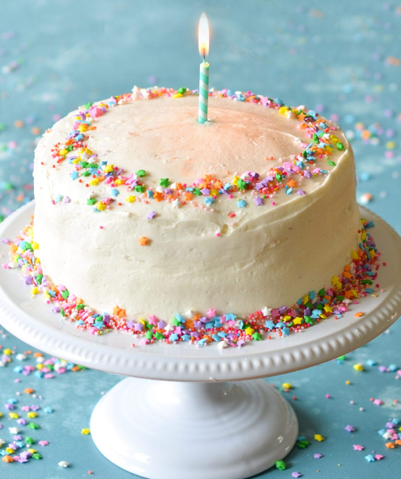 Photo of a birthday cake on a pedestal with one candle in the center