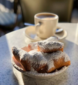 A plate of sugar-covered beignets on a table, with a mug of coffee in the background