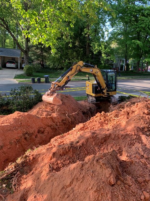 An excavator digs a trench across my front yard.