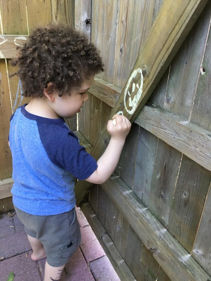 Small child drawing on a fence in chalk